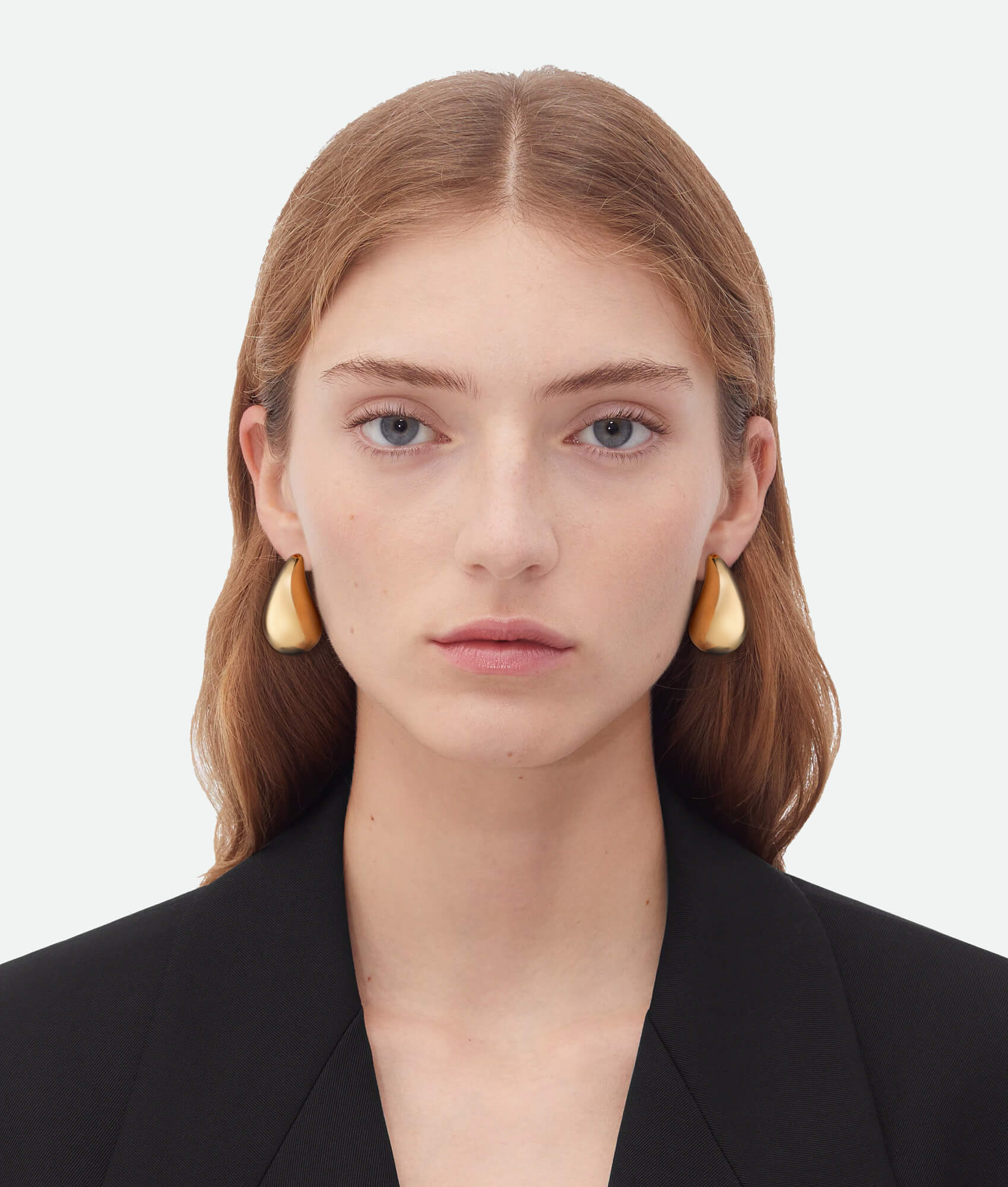 Woman wearing gold earrings against a plain background