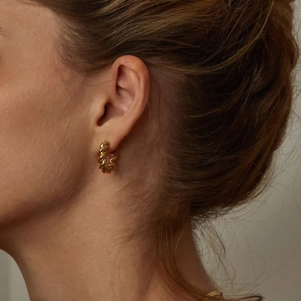 Close-up of a person wearing a gold hoop earring with a neutral background