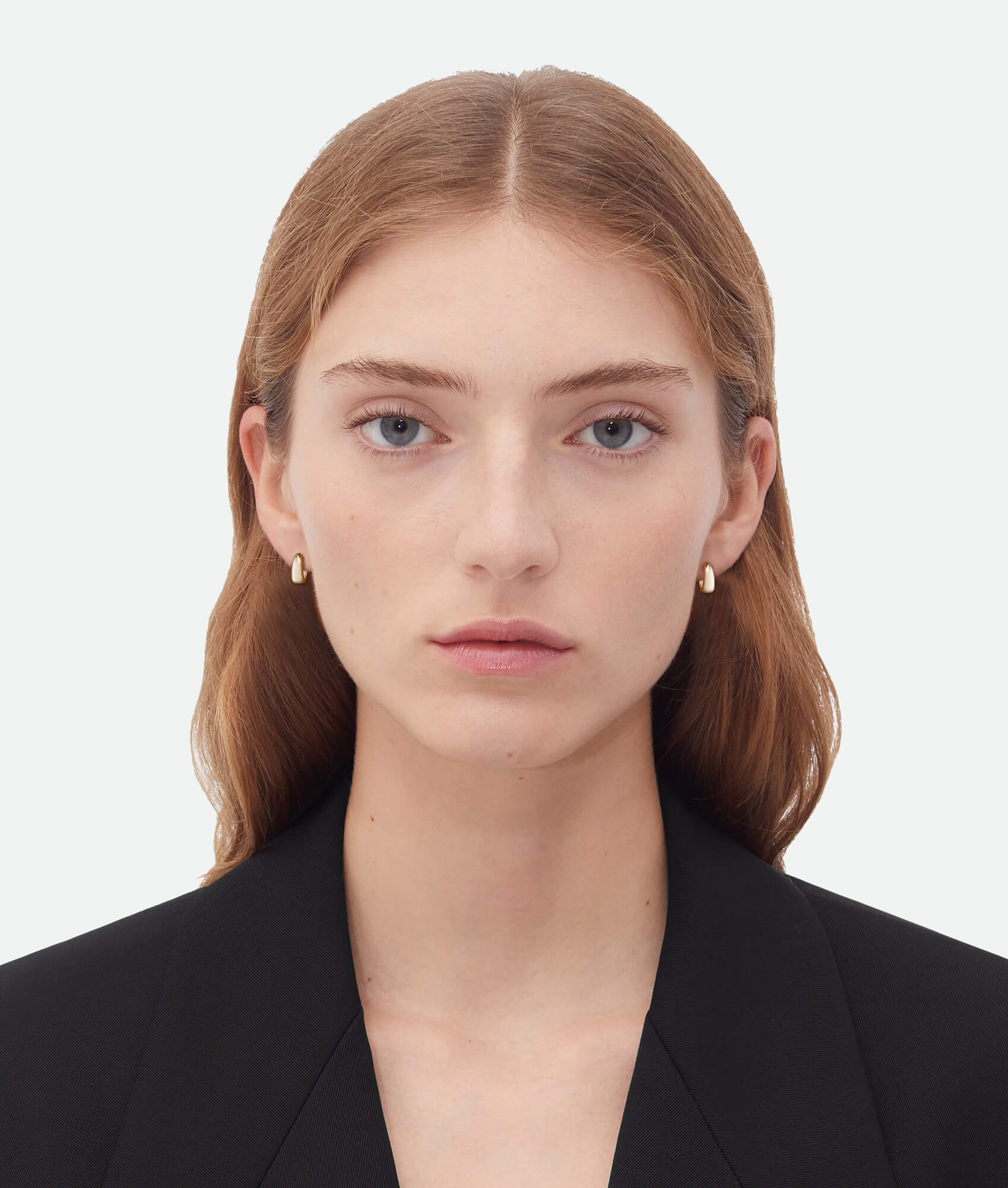 Woman wearing gold earrings against a plain background